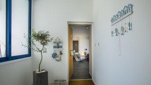 A hallway with a potted plant, a welcome sign, and a view into a room with a chair and a table. - Aster Suite in Protaras (Paralimni)
