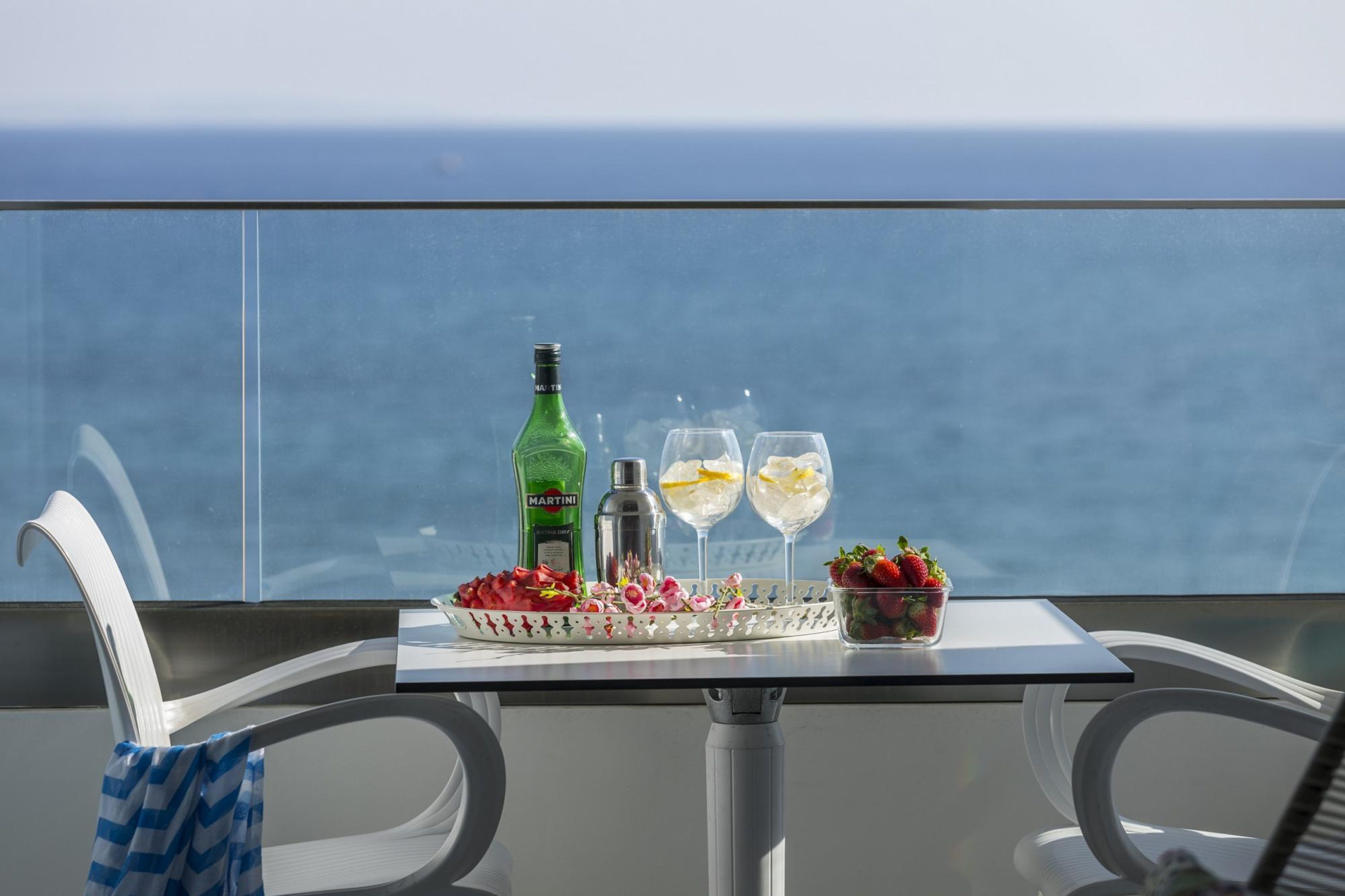 A table with a bottle, two glasses, a tray with strawberries, and a small bowl of flowers.