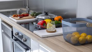 A kitchen counter with a cutting board, a glass of water, a bowl of lemons, and a mesh basket. - Mackenzie Zoe Seafront Suite (Larnaca)