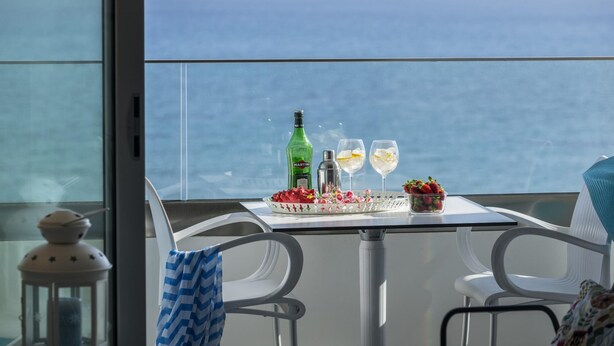 A table with a martini bottle, two glasses, strawberries, and a cocktail shaker on a balcony with a view of the ocean. - Mackenzie Zoe Seafront Suite (Larnaca)