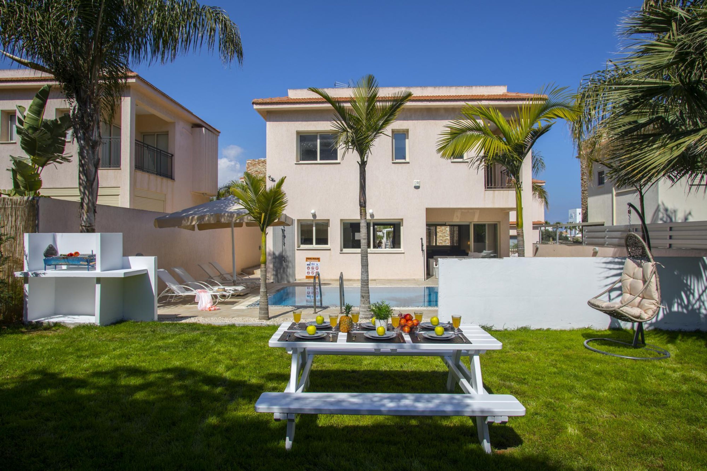 A poolside dining area with a table set for two, surrounded by palm trees and a building with balconies.