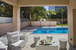 An outdoor pool area with a white sofa, wicker chairs, and a table with drinks and fruits. - Protaras Villa Michelle 10 (Paralimni)