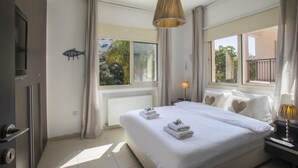 Une chambre moderne avec un grand lit, une table de chevet avec une lampe et une vue sur l’extérieur grâce à de grandes fenêtres.