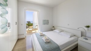A modern bedroom with a large bed, a bedside table, a nightstand, and a view of the outdoors. - Protaras Villa Kalena (Paralimni)