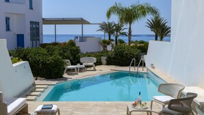 A poolside area with a clear view of the sea, lounge chairs, and a small table with a bottle. - Protaras Villa Kalena (Paralimni)