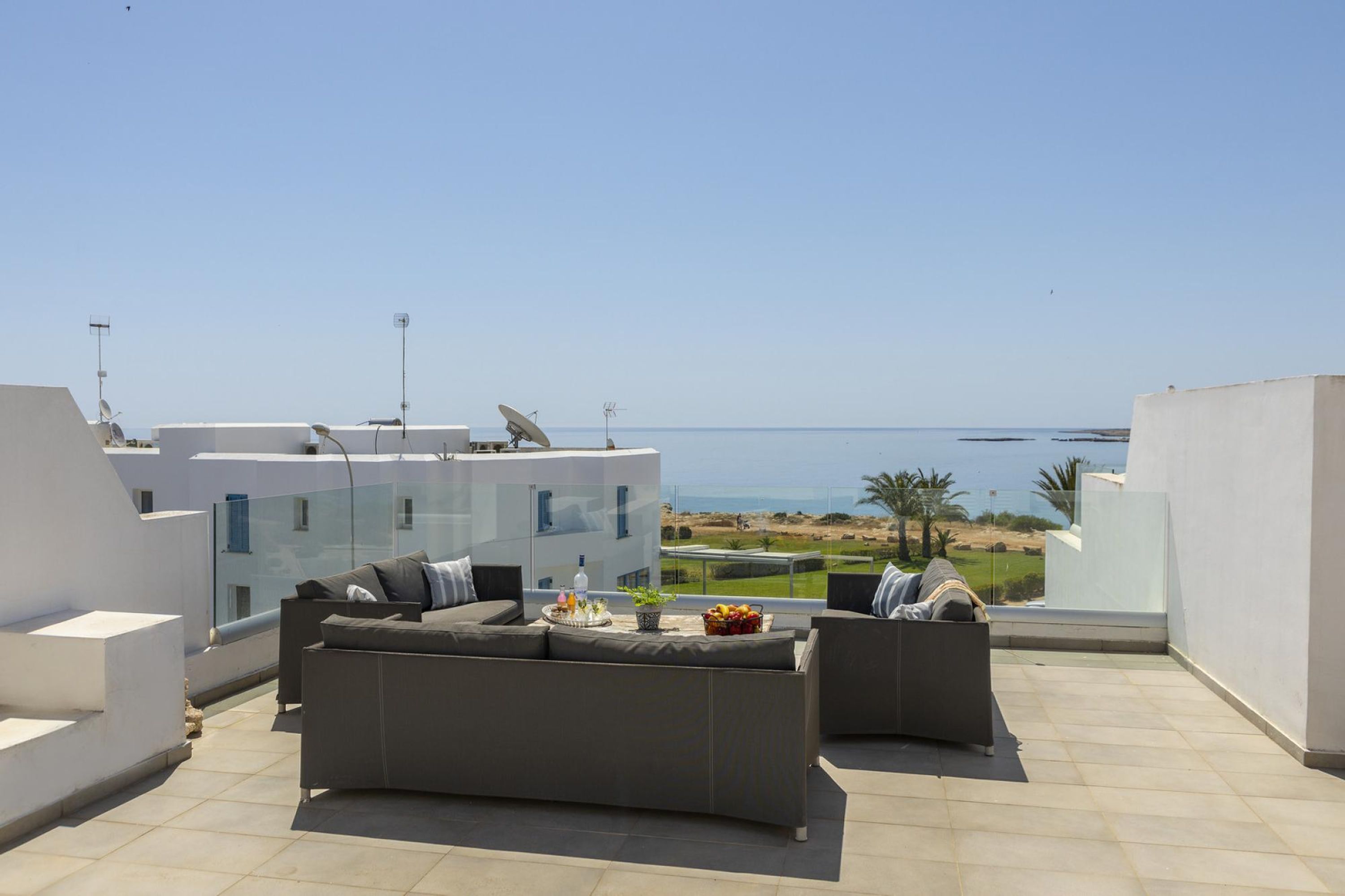 Une terrasse sur le toit avec un ensemble de canapés, un plateau de fruits et une bouteille, et une vue sur la mer.