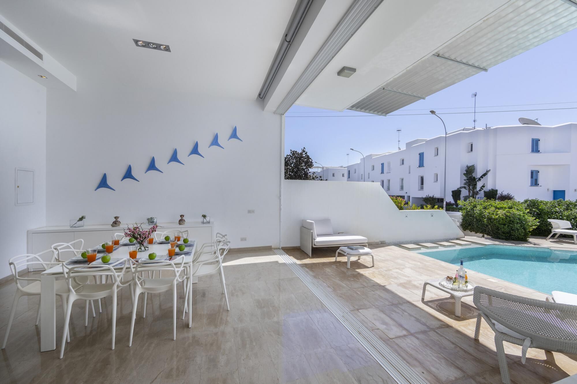 A modern outdoor area with a pool, white furniture, and a dining setup.