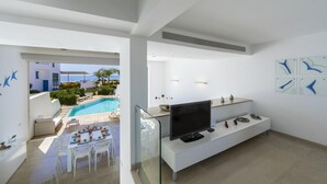A modern living room with a flat-screen TV, a glass coffee table, and a dining area with white furniture. - Protaras Villa Kalena (Paralimni)