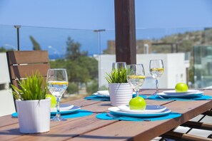 A table set for a meal with plates, glasses, and a potted plant on a wooden deck with a view of the sea. - Villa Anemoni Protaras (Paralimni)