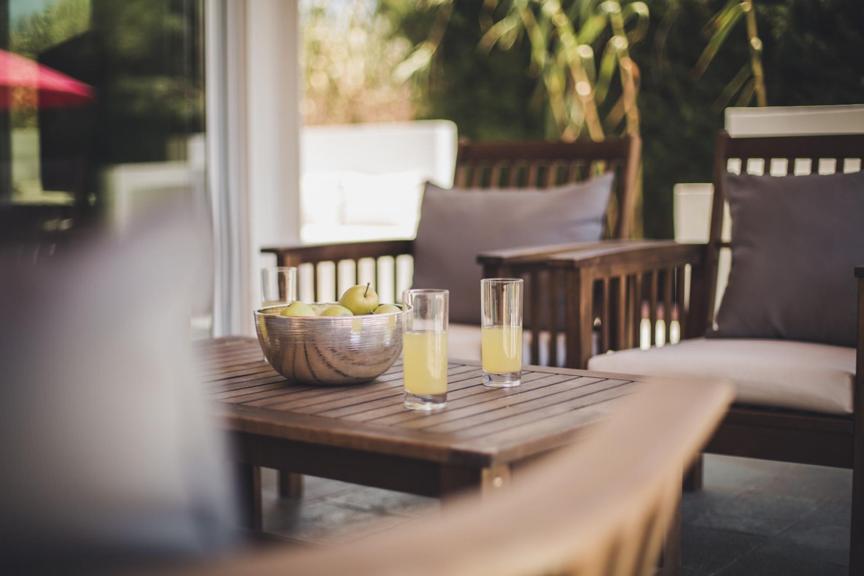 A wooden table with a bowl of fruit and two glasses of a yellow beverage.