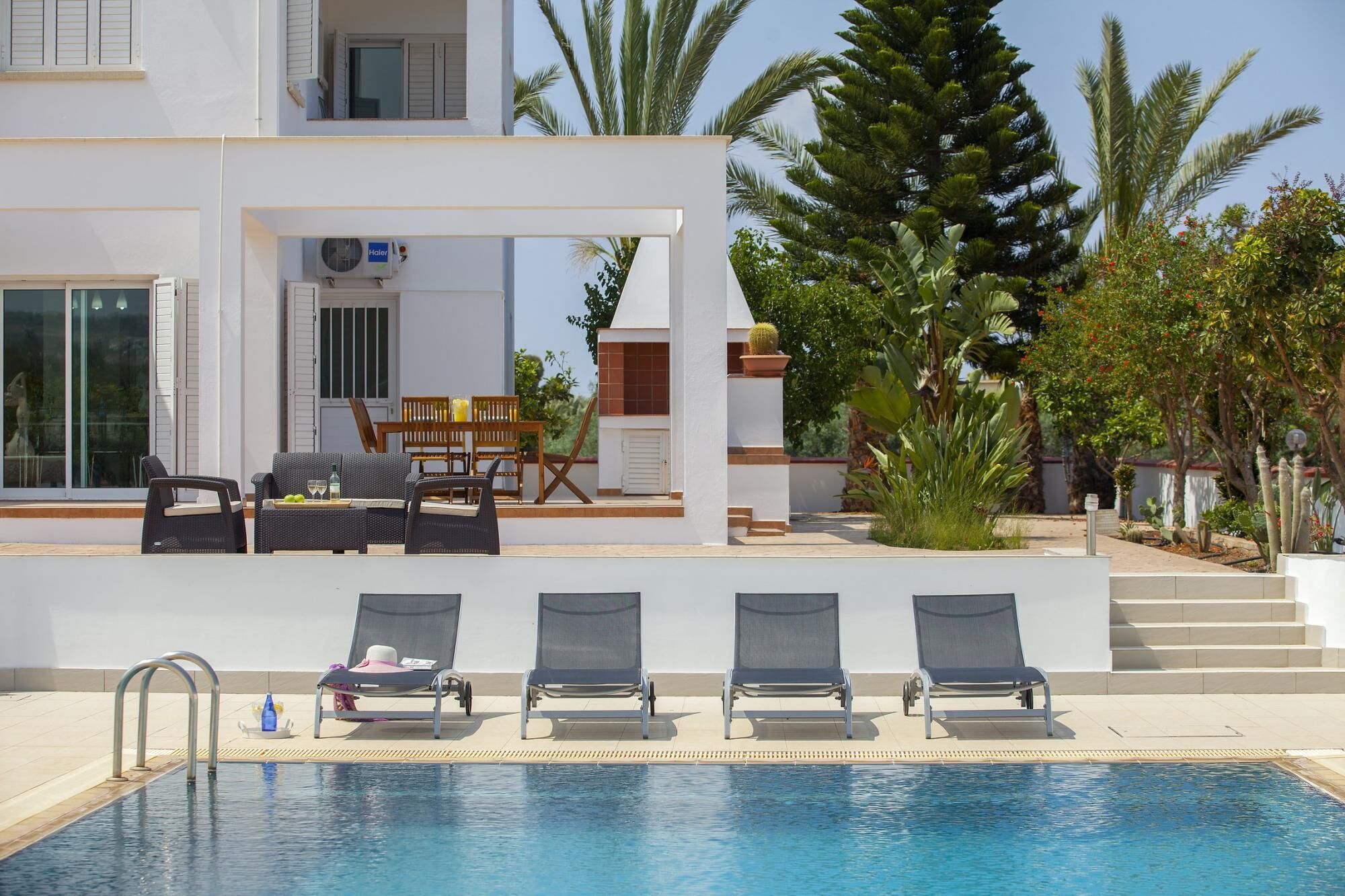 A poolside area with lounge chairs, a table with drinks, and a staircase leading to a covered patio.