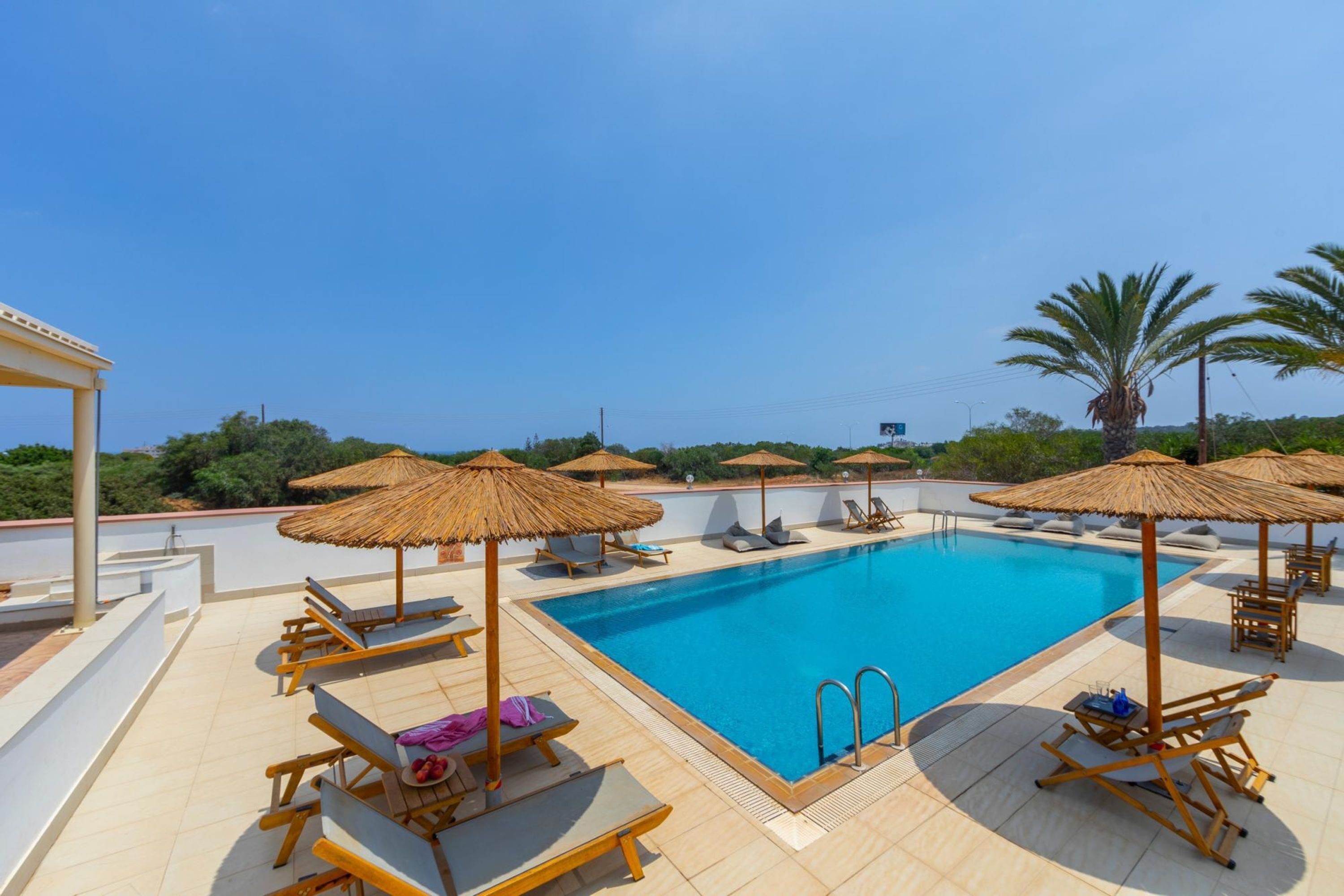 A rooftop pool area with lounge chairs, umbrellas, and a clear blue sky.