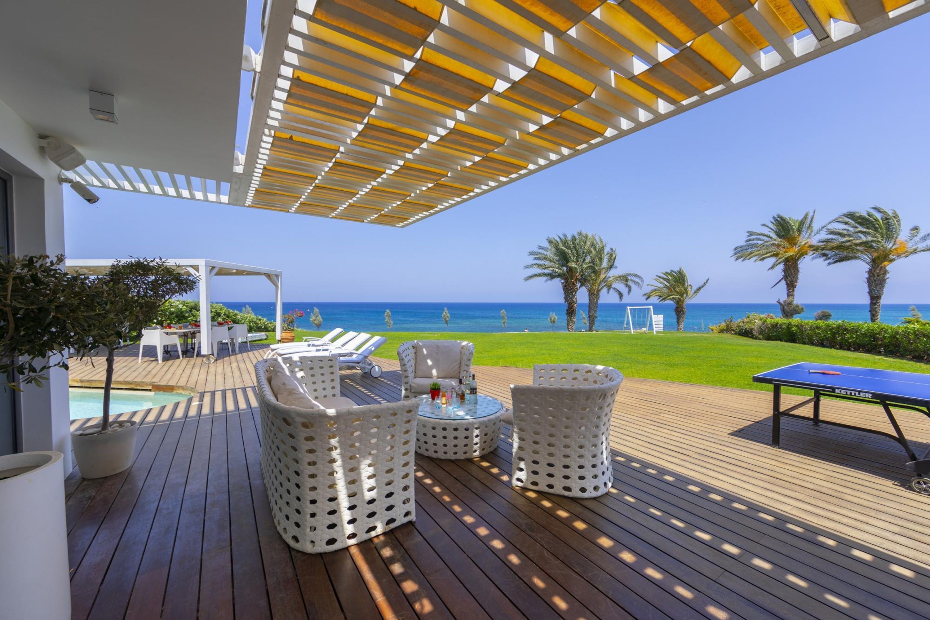 A deck with outdoor furniture, a ping pong table, and a view of the sea.