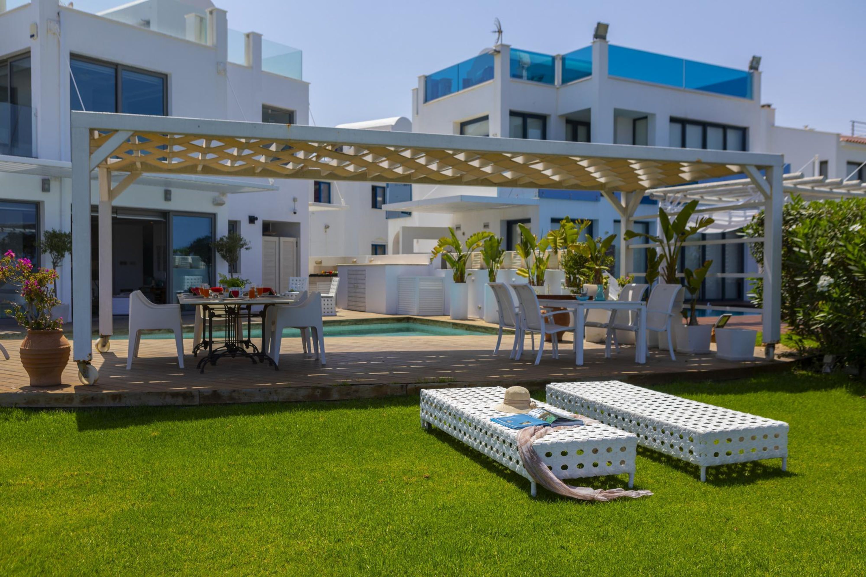 A modern outdoor patio area with a pool, white lounge chairs, and a pergola.