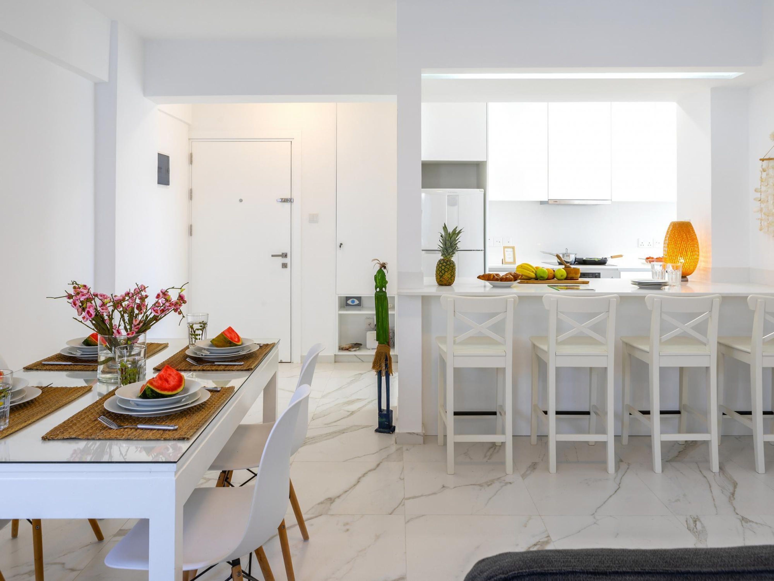 Una cocina moderna con armarios blancos, un comedor con mesa de vidrio y una isla de cocina con asientos.