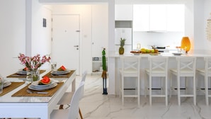 A modern kitchen with white cabinets, a dining area with a glass table, and a kitchen island with seating.
