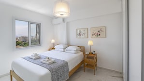 A modern bedroom with a bed, bedside lamps, a nightstand, and artwork on the wall.