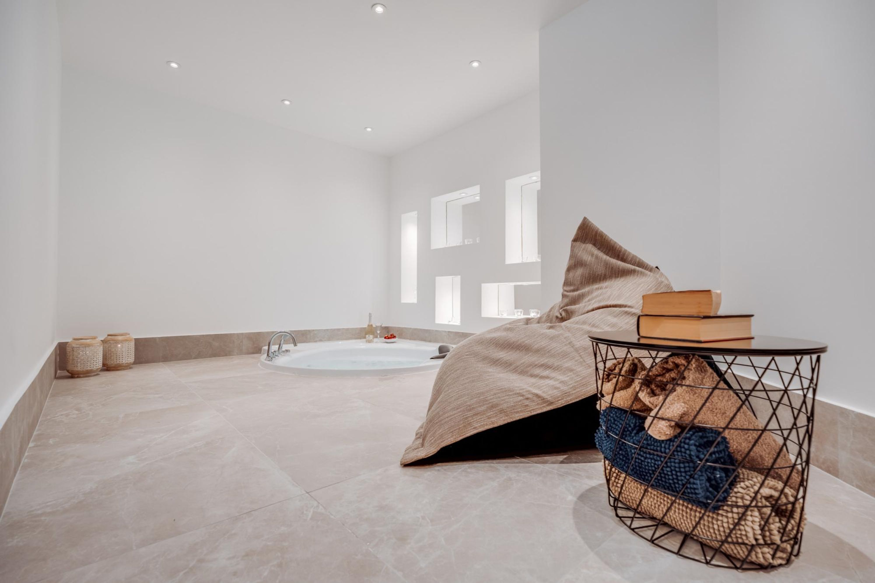 Une salle de bain moderne avec une baignoire, une petite table ronde sur laquelle repose un livre, et un grand fauteuil en forme de poire de couleur beige.