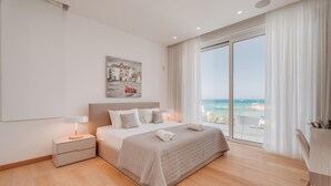 Um quarto de hotel moderno com uma cama grande, mesa de cabeceira, escrivaninha e vista para o mar.