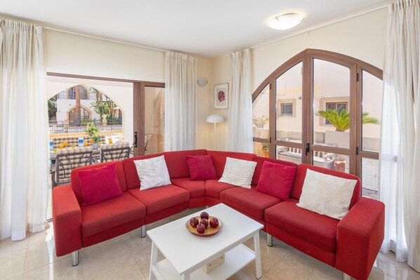 A modern living room with a red sectional sofa, a white coffee table, and large windows offering a view of the outside.
