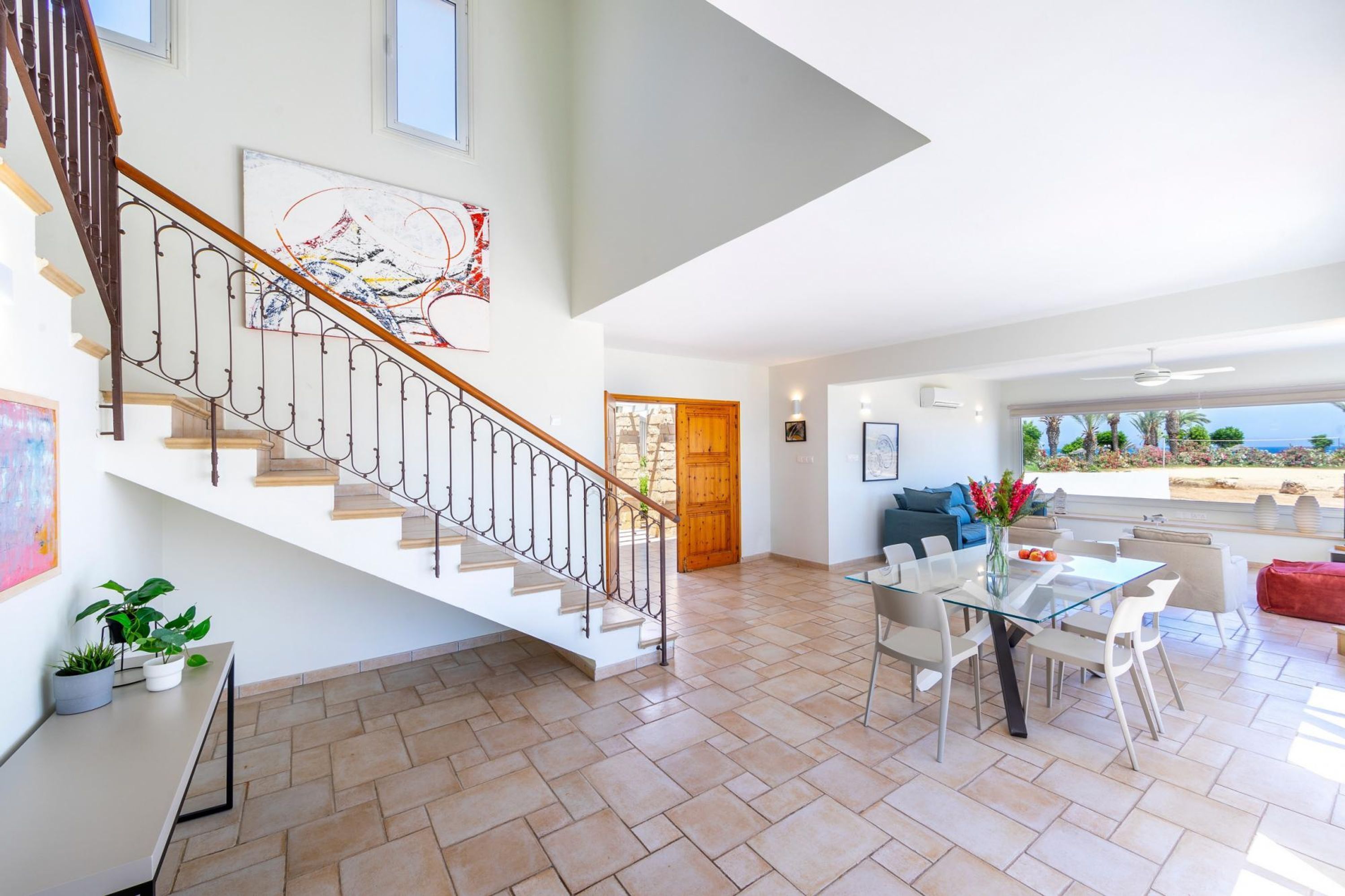 A spacious living area with a staircase, a dining table, and a view of the outdoors.