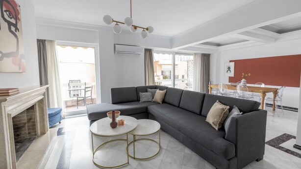 A modern living room with a grey sectional sofa, two round tables with gold frames, a fireplace, and a dining area with a wooden table and chairs. - Deco Marble Apt With Acropolis View (Athens)