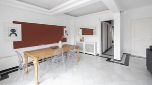 A dining area with a wooden table and clear chairs, white walls, and a red accent wall. - Deco Marble Apt With Acropolis View (Athens)