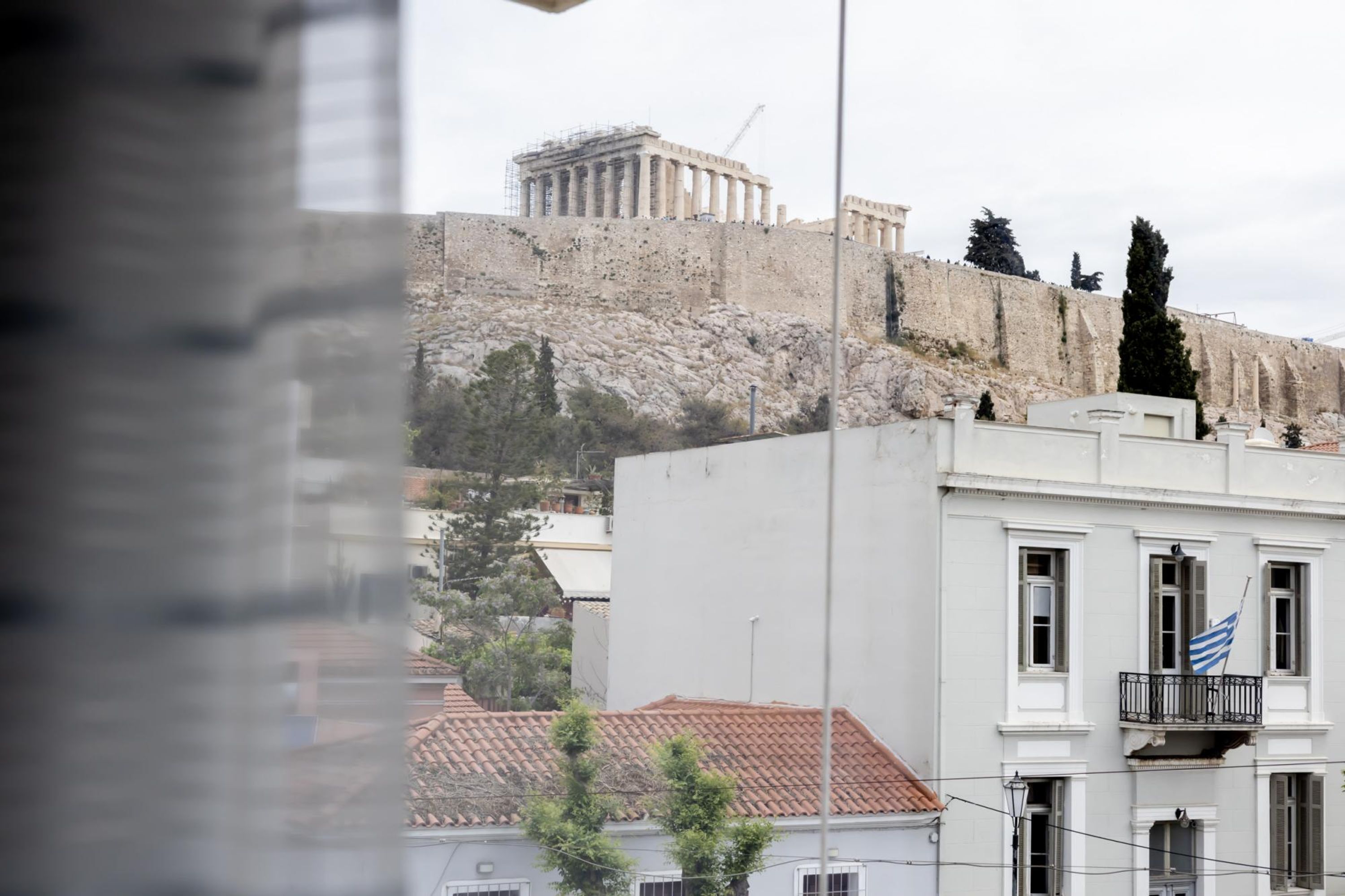 Vista d'un edifici amb un balcó i una bandera, davant d'un lloc històric amb columnes i una grua de construcció.