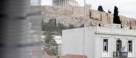 Blick auf ein Gebäude mit Balkon und einer Flagge, vor einer historischen Stätte mit Säulen und einem Baukran.