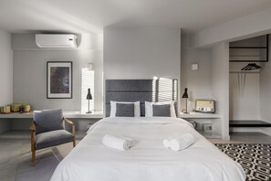 A modern hotel room with a large bed, a desk with a lamp, a chair, and a window with blinds. - Fantastic Central Athens Suite With Rooftop Deck (Athens)