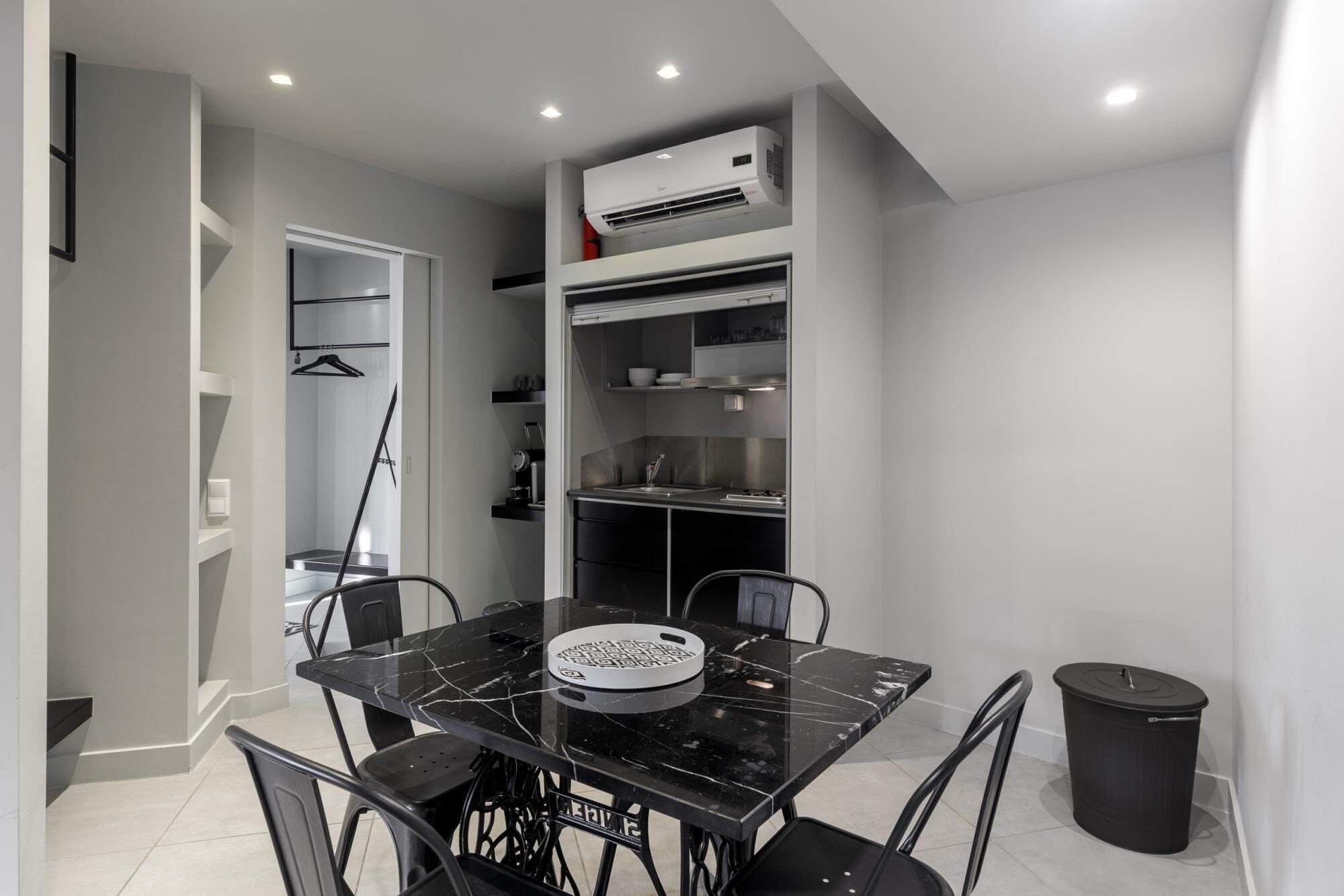A modern kitchen with a black marble countertop, a built-in stove, and a small sink. There is a black trash bin to the right and a white air conditioning unit above the stove.