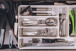 Een keukenaccessoire-organizer met vakken voor lepels, vorken, messen en ander keukengerei.