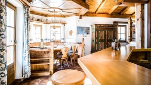 A rustic wooden interior with a high ceiling, a wooden bar area, and a seating space with chairs and a table. - Landhaus Lodges Kaprun - Johann (Kaprun)