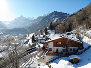 A snow-covered mountain village with houses, a wooden cabin, and a clear view of the surrounding mountains.