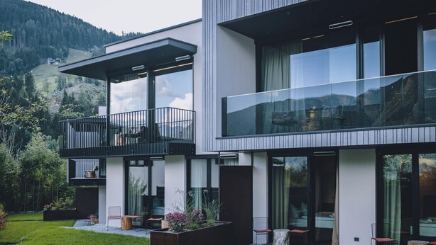 Une maison moderne à deux étages, dotée d’un balcon, de grandes fenêtres et d’un jardin bien entretenu.