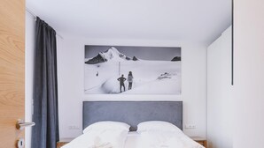 Een hotelkamer met een bed, een groot schilderij van een besneeuwd berglandschap en een houten deur.