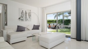 Ein modernes Wohnzimmer mit einem weißen Sofa, einem Glastisch und einem großen Fenster mit Blick auf einen Garten.