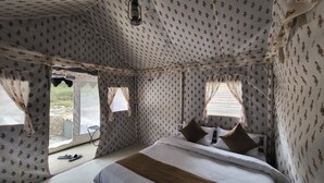 Una habitació amb cortines estampades, un llit amb almoades i una finestra amb vista a l'exterior.