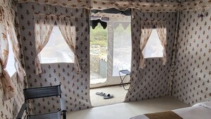 Una habitació tipus tenda amb un llit, una cadira plegable i una taula petita.