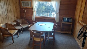 L’intérieur d’une cabane en bois comprend une table à manger, quatre chaises, une petite télévision et un ventilateur.