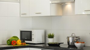 Una cocina moderna con armarios blancos, un microondas, una estufa y diversos utensilios de cocina.