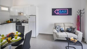 Una cocina moderna con armarios blancos, un comedor con una mesa para dos personas y una sala de estar con un sofá y una mesa de centro.