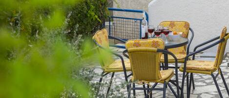 A patio with wicker chairs and a table, a blue shopping cart, and a bottle of wine.