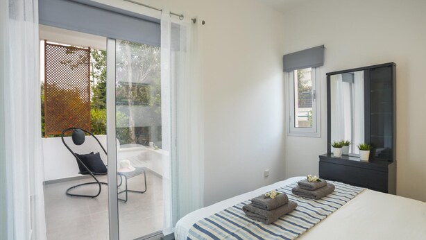Un dormitorio moderno con una cama grande, una puerta corrediza de vidrio que da a un área de estar exterior, un aparador oscuro y un espejo.
