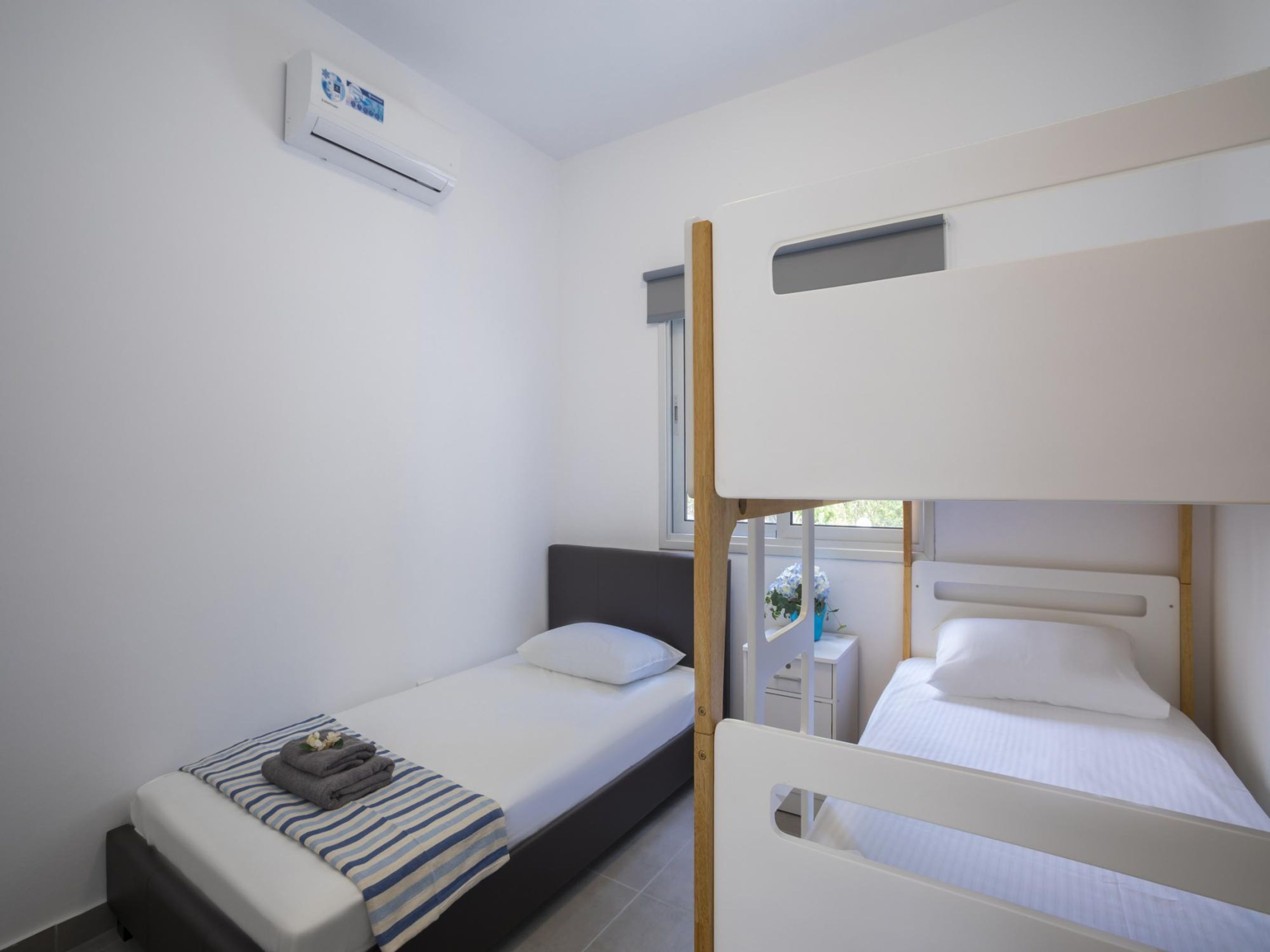 Una habitación pequeña y limpia con dos camas individuales, una mesita de noche y un equipo de aire acondicionado en la pared.
