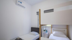 Una habitación pequeña y limpia con dos camas individuales, una mesita de noche y un equipo de aire acondicionado en la pared.
