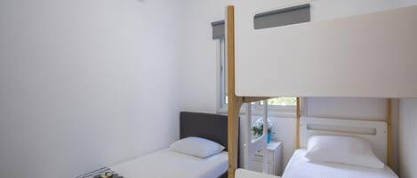 Una habitación pequeña y limpia con dos camas individuales, una mesita de noche y un equipo de aire acondicionado en la pared.