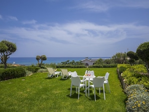 A well-maintained outdoor area with a table and chairs, a view of the sea, and a building in the background.