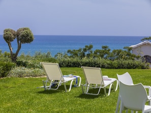 A grassy area with three white lounge chairs facing a view of the sea.