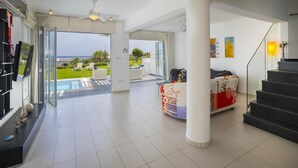 A spacious living area with a large glass door leading to a balcony overlooking a green landscape and the sea. - Protaras Seafront Villa Sirina Pearl (Paralimni)